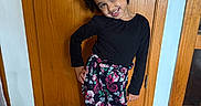 Serenity joined the competition — help win amazing prizes! black_shirt, child, curly_hair, face, fashion, floral_pants, full_body, girl, hallway, happy, hardwood_floor, home, indoor, photography, playful_pose, portrait, shoes, smiling, standing, wooden_door