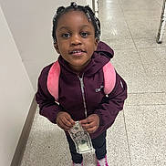 Kamiyah joined the competition — help win amazing prizes! child, girl, smiling, portrait, standing, indoor, hallway, tile_floor, backpack, pink_backpack, braided_hair, jacket, purple_clothing, sneakers, money, dollar_bill, hands, schoolchild, front_facing, happy