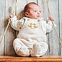 baby, child, swing, rope, wooden_swing, wooden_background, indoor, white_clothing, cute, infant, seated, portrait, cozy, playful, hands, face, eyes, buttoned_outfit, soft_texture, photography