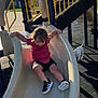 black_shorts, black_surface, child, clothing, daylight, dog, fun, outdoor, park, pet, plastic_slide, play_equipment, playground, red_shirt, shadow, shoes, slide, sunlight, toddler, yellow_rails