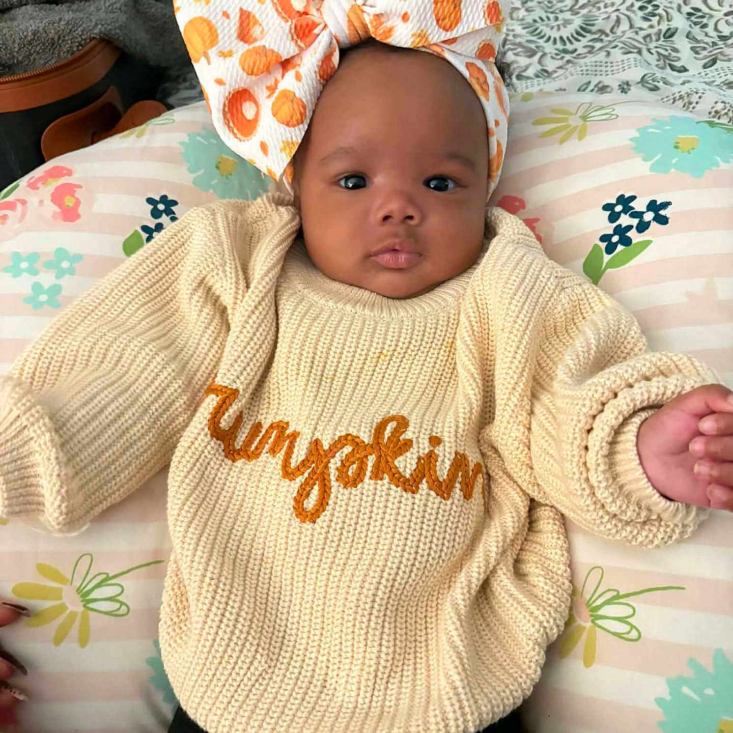 Nye'L is registered to the contest to win money with this photo: baby, bedspread, blanket, bow, child, clothing, comfortable, cream, cushion, cute, floral_pattern, headband, indoors, infant, knitted_sweater, lying_down, orange, person, portrait, soft