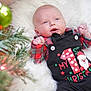 baby, infant, christmas, holiday, festive_clothing, plaid, black_overalls, santa_claus, white_blanket, christmas_tree, ornament, green, red, smiling, cute, indoor, celebration, portrait, child, seasonal