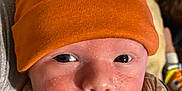 Spencer is registered to the contest to win money with this photo: baby, blanket, child, close_up, clothing, cute, expression, eyes, face, hat, headwear, indoors, infant, mouth, newborn, orange_hat, person, portrait, skin, wrapped