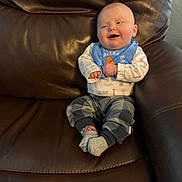 Spencer is registered to the contest to win money with this photo: baby, infant, smiling, sitting, leather_chair, bib, socks, onesie, plaid_pants, recliner, cozy, candid, portrait, cute, laughter, hands, feet, upholstery, home_interior, infant_clothing