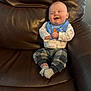 baby, infant, smiling, sitting, leather_chair, bib, socks, onesie, plaid_pants, recliner, cozy, candid, portrait, cute, laughter, hands, feet, upholstery, home_interior, infant_clothing