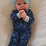 baby, infant, child, headband, bow, onesie, blue_clothing, floral_pattern, blanket, textured_blanket, hands, cute, lying_down, portrait, indoors, face, expression, clothing, person, adorable