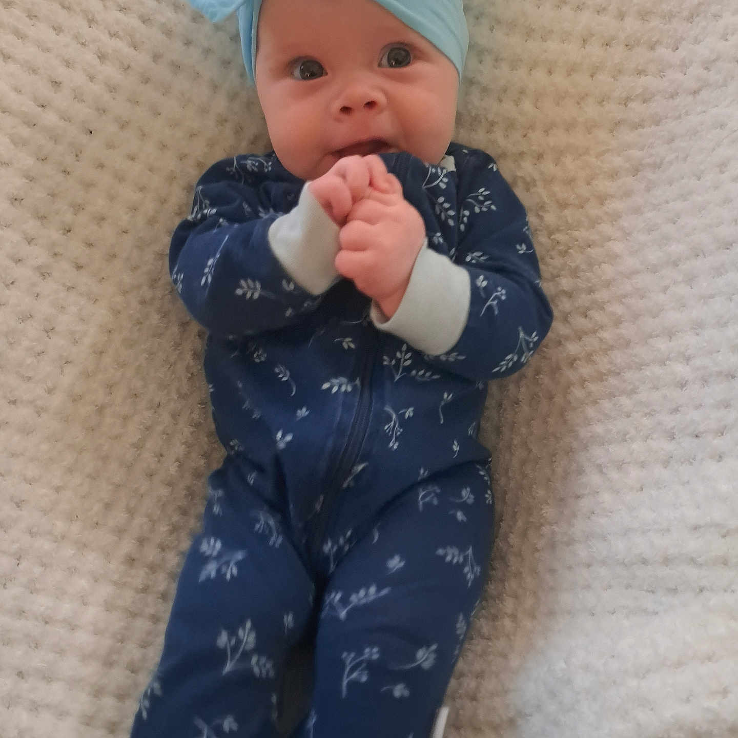 Annabelle joined the competition — help win amazing prizes! baby, infant, child, headband, bow, onesie, blue_clothing, floral_pattern, blanket, textured_blanket, hands, cute, lying_down, portrait, indoors, face, expression, clothing, person, adorable