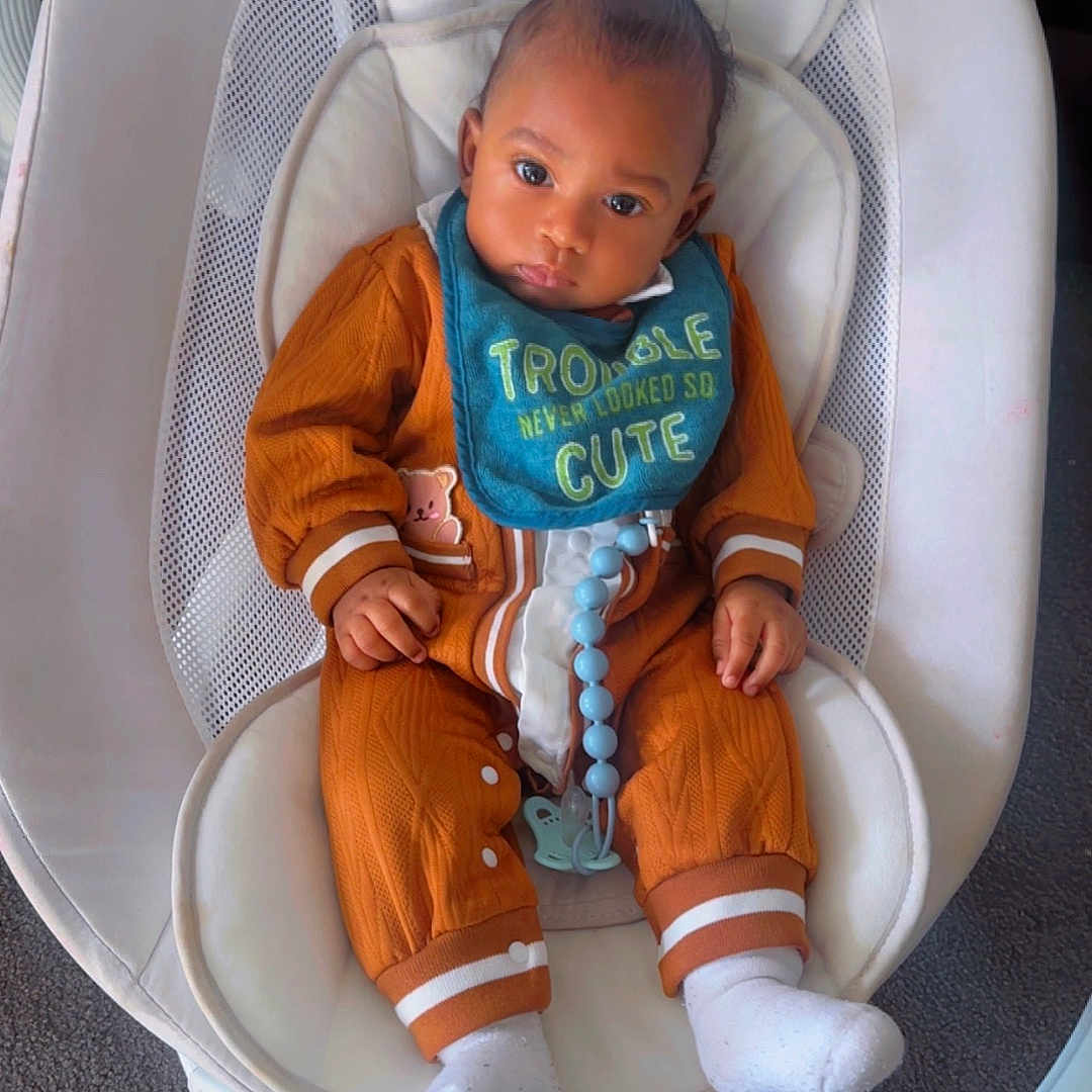 Jaaziel joined the competition — help win amazing prizes! baby, infant, bib, orange_outfit, baby_rocker, baby_seat, white, child, indoor, carpet, footwear, socks, cute, portrait, young_child, comfort, expression, clothing, seated, adorable