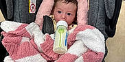 Scarlett is registered to the contest to win money with this photo: baby, infant, car_seat, blanket, bottle, feeding, face, person, indoors, floor_tiles, pink, white, gray, clothing, newborn, cute, child, soft_texture, wrapped, captive