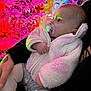 Lyra is registered to the contest to win money with this photo: baby, pacifier, white_jacket, christmas_tree, pink_lights, red_lights, festive, holiday, child, infant, cozy, warm_clothing, indoor, colorful, glowing_lights, person, holding, soft_texture, cute, curious