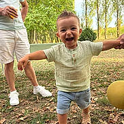 Augustin participe au concours pour gagner de l'argent avec cette photo : adult, ball, child, daylight, family, grass, hand_holding, happy, leaves, nature, outdoor, person, sandals, shirt, shorts, smiling, summer, toddler, trees, walking