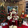 santa_claus, child, toddler, christmas_tree, christmas_decorations, nutcracker, red_carpet, holiday, festive, ornaments, beanie, pacifier, indoor, person, smile, white_beard, gift_box, holiday_season, chair, winter_clothing