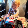 Waylon joined the competition — help win amazing prizes! toddler, child, toy_car, pacifier, chair, blanket, indoor, blond_hair, short_sleeve_shirt, playing, seat, young_child, person, furniture, casual_clothing, curious, hands, light, home, relaxed