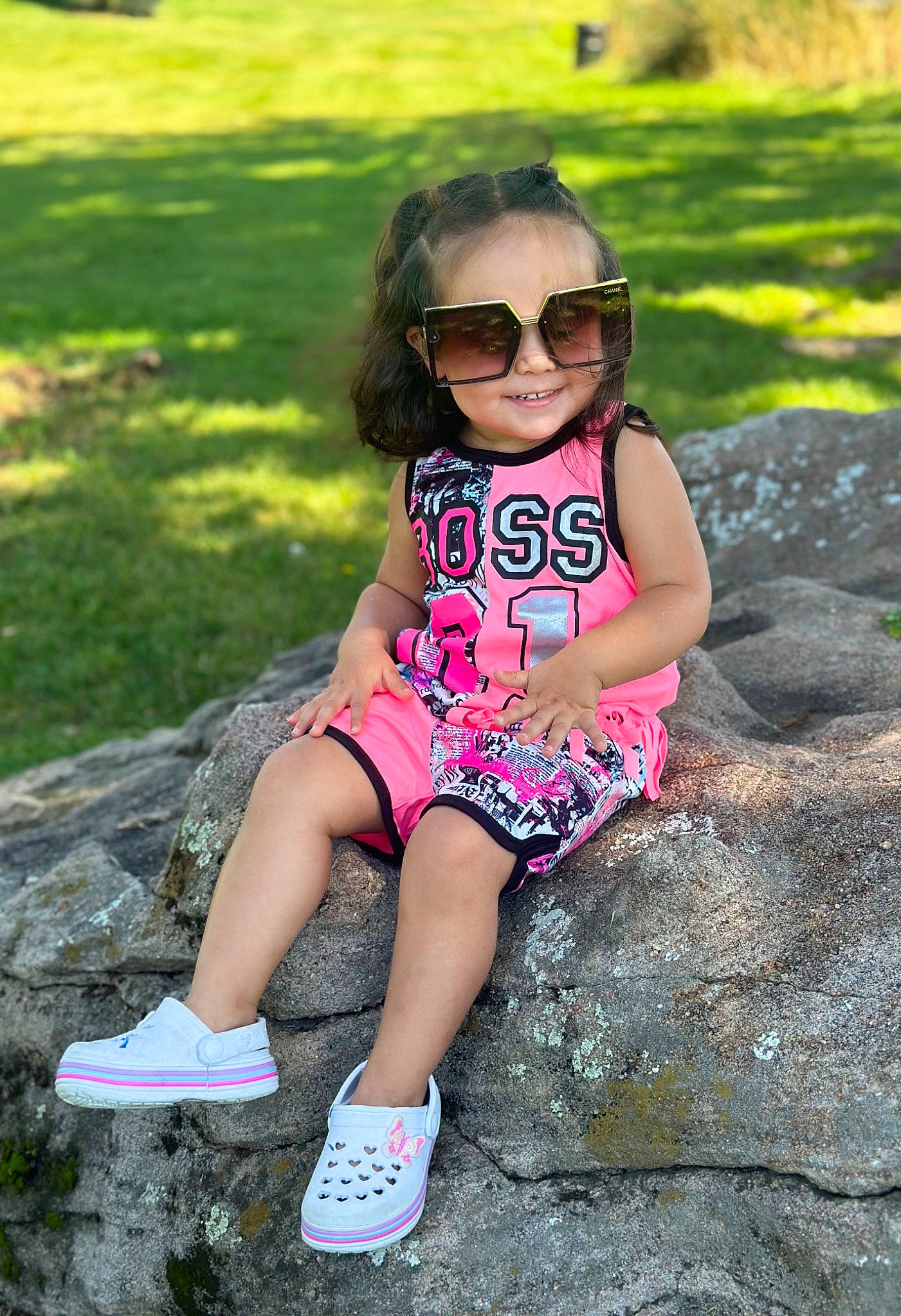 Emberly is registered to the contest to win money with this photo: baby_toddler_clothing, cool, eyewear, face, footwear, glasses, goggles, grass, happy, joy, leaf, leisure, people_in_nature, person, pink, plant, shoe, smile, sneakers, sunglasses