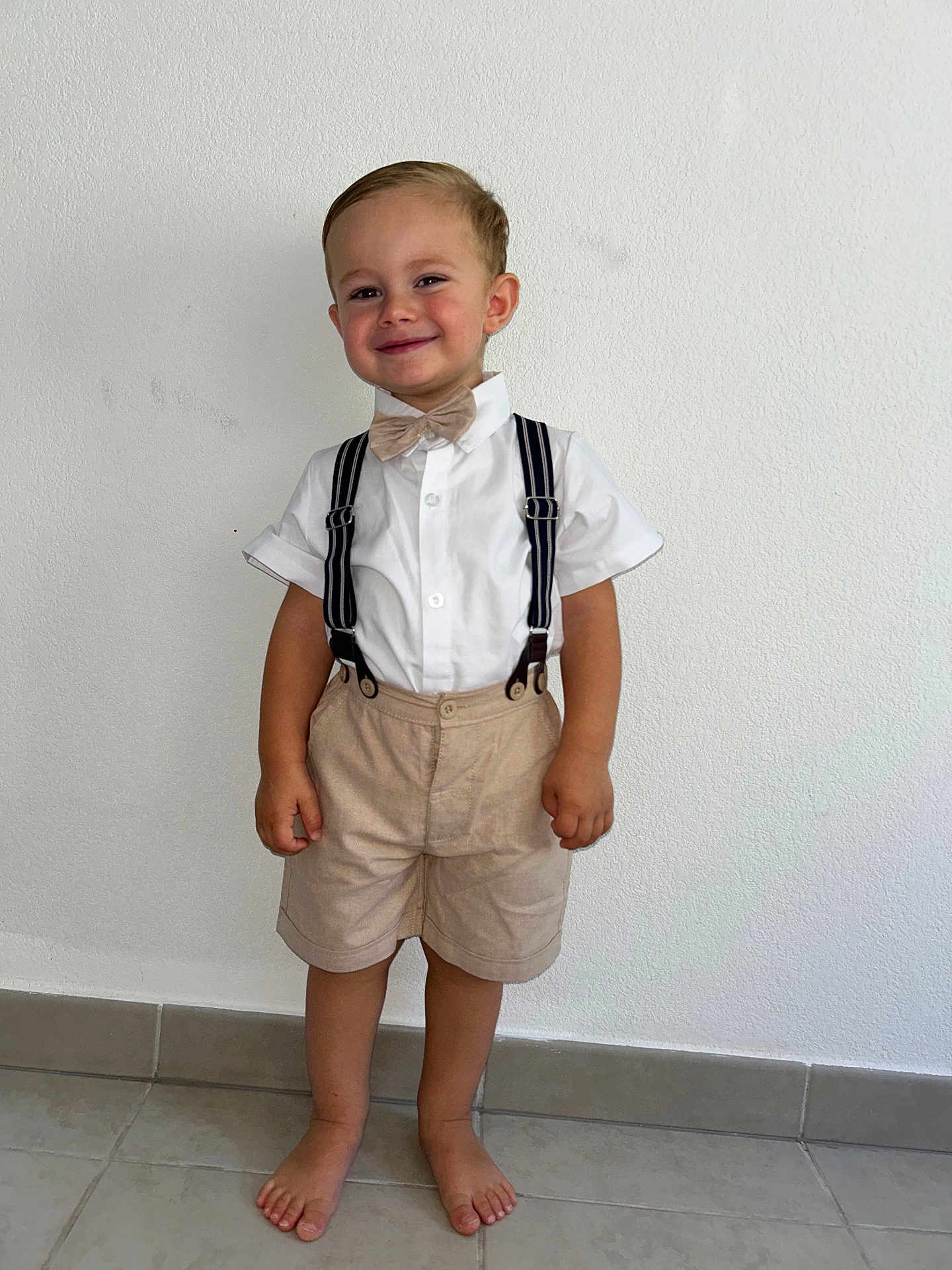 Giuliann a rejoint le concours — aidez-le/la à gagner de superbes lots ! child, boy, smile, barefoot, shorts, suspenders, bow_tie, white_shirt, standing, tile_floor, indoor, casual, cute, happy, portrait, fashion, person, minimalist_background, light, clothing