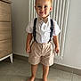 Giuliann a rejoint le concours — aidez-le/la à gagner de superbes lots ! child, boy, barefoot, curly_hair, white_shirt, bow_tie, suspenders, beige_shorts, indoor, tiled_floor, radiator, smile, standing, portrait, casual, young, cute, person, home, fashion