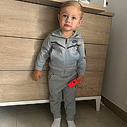 Giuliann participe au concours pour gagner de l'argent avec cette photo : toddler, child, grey_tracksuit, nike, controller, red_controller, barefoot, socks, standing, wooden_dresser, baby_changing_pad, indoor, floor_tiles, curious_expression, short_hair, casual_clothing, person, room_interior, furniture, young_child