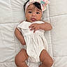 baby, infant, child, portrait, lying_down, white_dress, floral_headband, bow, blanket, quilt, indoor, fashion, cute, tongue_out, smiling, face, eyes, hands, feet, photography