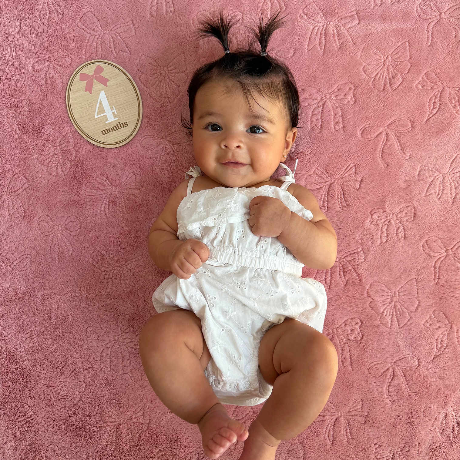 Giovanna is registered to the contest to win money with this photo: baby, infant, child, four_months, portrait, lying_down, smiling, face, white_outfit, pink_blanket, bow_pattern, hair_bows, ponytails, indoors, baby_photography, milestone, four_month_milestone, cute, playful, sitting_pose