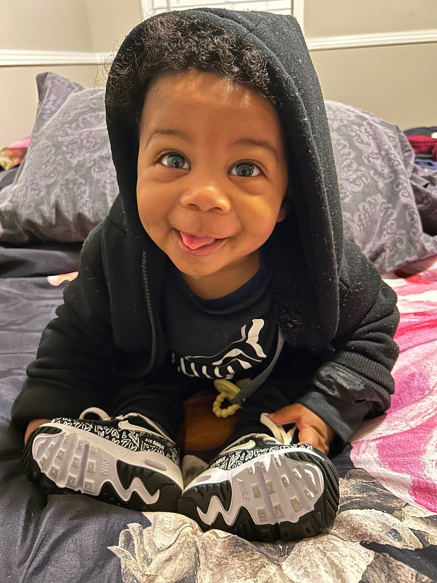 Chozyn is registered to the contest to win money with this photo: bed, black_clothing, casual_clothing, child, cozy, curly_hair, cute, happy, hoodie, indoors, nike_shoes, person, pillow, playful, portrait, smiling, sneakers, toddler, tongue_out, young_child