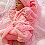 Kamora is registered to the contest to win money with this photo: baby, pink_robe, slippers, blanket, infant, cozy, sleepwear, soft_texture, lying_down, cute, child, warm_clothing, indoors, portrait, newborn, resting, wrapped, comfortable, adorable, soft_lighting