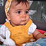 baby, child, headband, yellow, overalls, plush_toys, indoor, plant, decor, curious, seated, soft_toys, face, clothing, cute, portrait, toddler, furniture, expression, person