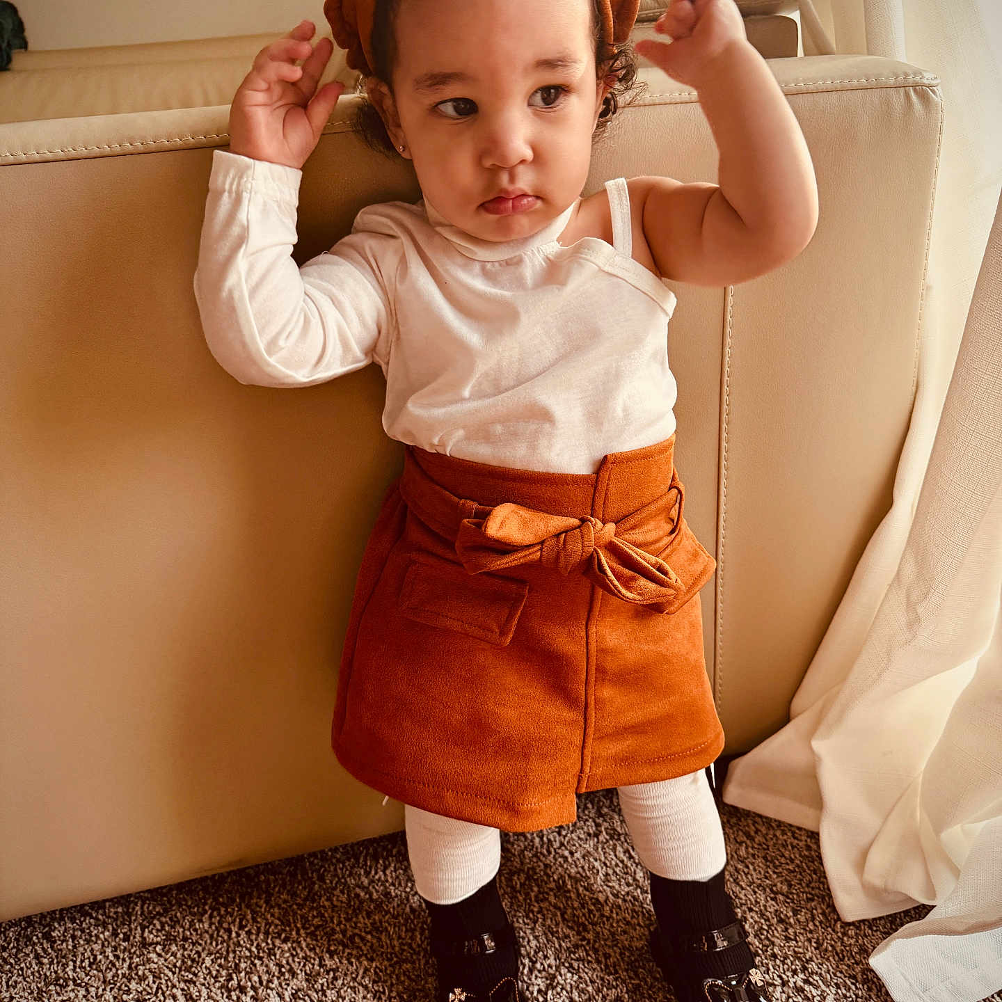 Young Mula is registered to the contest to win money with this photo: beret, black_shoes, carpet, child, couch, curly_hair, cute, expression, fashion, hands_up, home, indoor, neutral_colors, person, portrait, skirt, standing, toddler, white_top, window_curtains