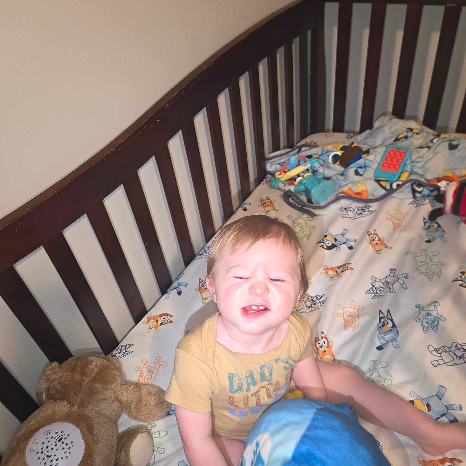 Axel joined the competition — help win amazing prizes! toddler, crib, bed, blanket, toy, stuffed_animal, child, face, smile, yellow_shirt, indoor, furniture, cartoon_print, baby, happy, light_skin, short_hair, play, sitting, cute