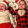 baby, infant, holiday_clothing, santa_hat, plaid, red_and_black, cream_sweater, blanket, pattern, truck_pattern, christmas_theme, cute, two_babies, lying_down, face, headwear, smiling_baby, serious_baby, indoors, cozy