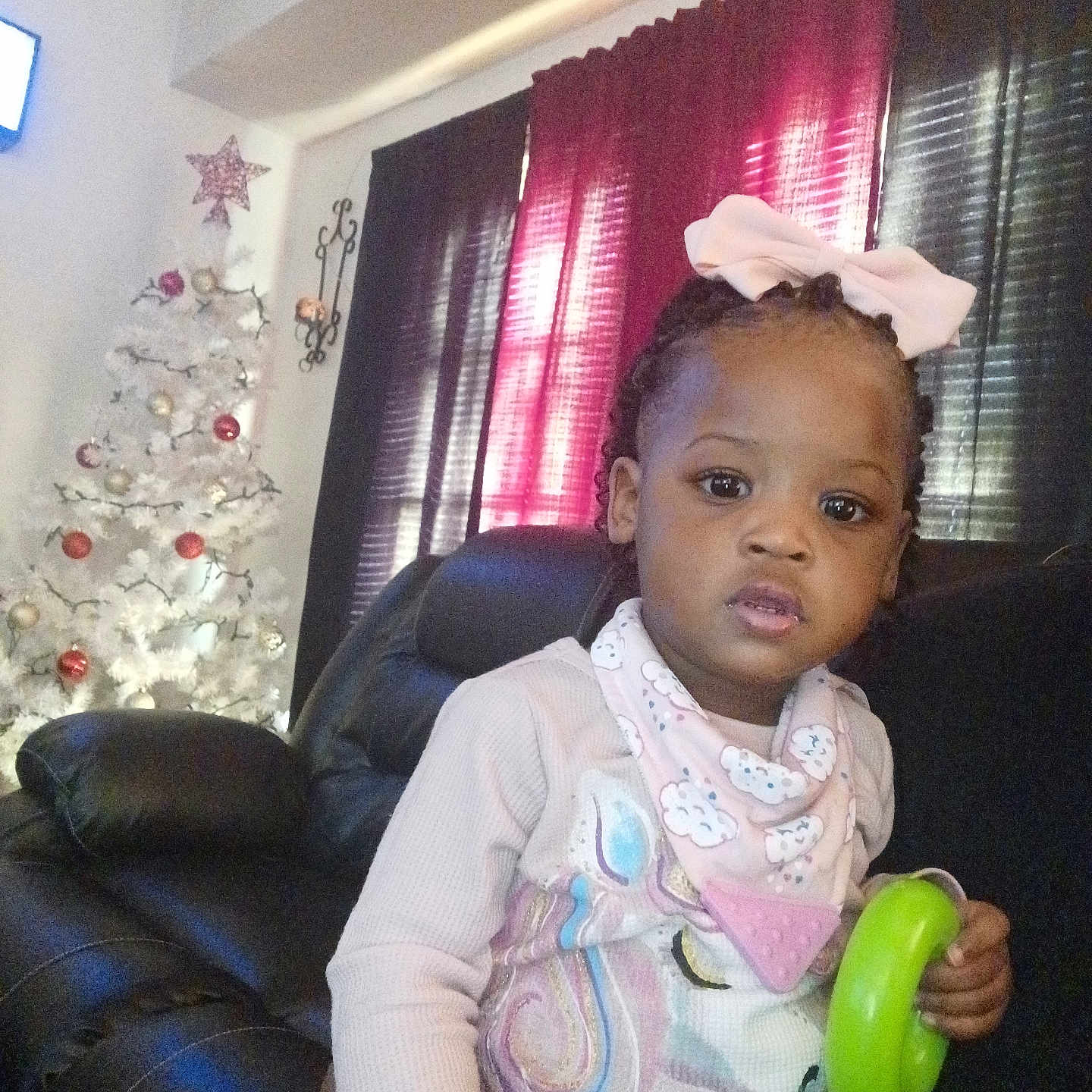 Royalty is registered to the contest to win money with this photo: toddler, child, girl, bow, braids, toy, chair, leather, christmas_tree, ornaments, holiday, indoor, curtain, window, pink, white, black, decor, portrait, casual