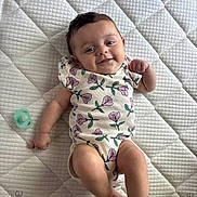 Jade joined the competition — help win amazing prizes! baby, infant, smiling, lying_down, onesie, floral_pattern, pacifier, quilted_mattress, child, cute, happy, skin, person, indoors, young_child, resting, baby_clothes, sleeping_area, comfort, playful