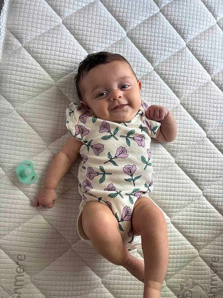 Jade joined the competition — help win amazing prizes! baby, infant, smiling, lying_down, onesie, floral_pattern, pacifier, quilted_mattress, child, cute, happy, skin, person, indoors, young_child, resting, baby_clothes, sleeping_area, comfort, playful