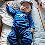 baby, infant, child, blue_clothing, cap, bed, cushion, indoor, casual, relaxed, face, hands, footwear, sneakers, expressionless, home, soft_lighting, portrait, resting, cozy