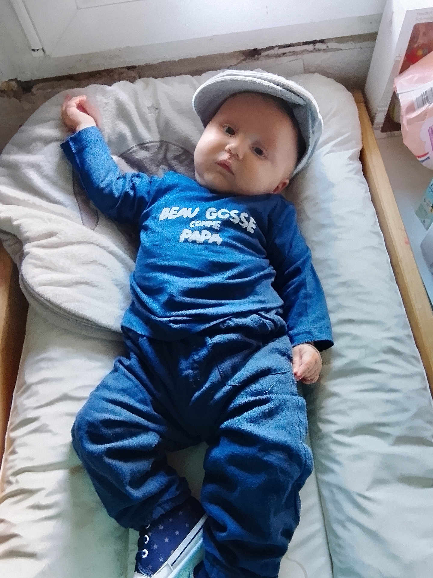 Kellyo participe au concours pour gagner de l'argent avec cette photo : baby, infant, child, blue_clothing, cap, bed, cushion, indoor, casual, relaxed, face, hands, footwear, sneakers, expressionless, home, soft_lighting, portrait, resting, cozy