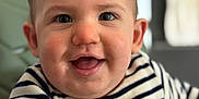 Ezio participe au concours pour gagner de l'argent avec cette photo : baby, infant, toddler, smiling, closeup, portrait, face, eyes, cheeks, drool, striped_shirt, lion_patch, highchair, indoor, bokeh, blurred_background, hair, ear, happy, cute