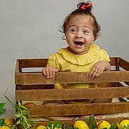 Daisy joined the competition — help win amazing prizes! baby, bright_colors, child, curly_hair, cute, decorative, fruit, green_leaves, happy, indoors, lemons, natural_light, plant, playful, portrait, sitting, smiling, toddler, wooden_crate, yellow_clothing