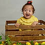 baby, bright_colors, child, curly_hair, cute, decorative, fruit, green_leaves, happy, indoors, lemons, natural_light, plant, playful, portrait, sitting, smiling, toddler, wooden_crate, yellow_clothing