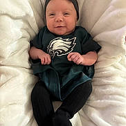 Kyla is registered to the contest to win money with this photo: baby, infant, smiling, headband, clothing, blanket, green, black, socks, person, cute, indoors, portrait, sports_team_logo, soft_texture, happy, seated, small_hands, cozy, newborn