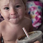 Xayden is registered to the contest to win money with this photo: toddler, child, face, expression, drink, straw, hand, tattoo, indoor, blanket, blurred_background, curly_hair, closeup, skin, portrait, young_child, beverage, plastic_cup, curious, casual