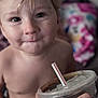 toddler, child, face, expression, drink, straw, hand, tattoo, indoor, blanket, blurred_background, curly_hair, closeup, skin, portrait, young_child, beverage, plastic_cup, curious, casual