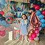 child, birthday, balloons, blue_dress, glasses, number_4_balloon, gift_bags, floor, marble_floor, party, celebration, stitch_character, pink_balloons, red_balloons, blue_balloons, decorations, smiling, indoor, curly_hair, happy