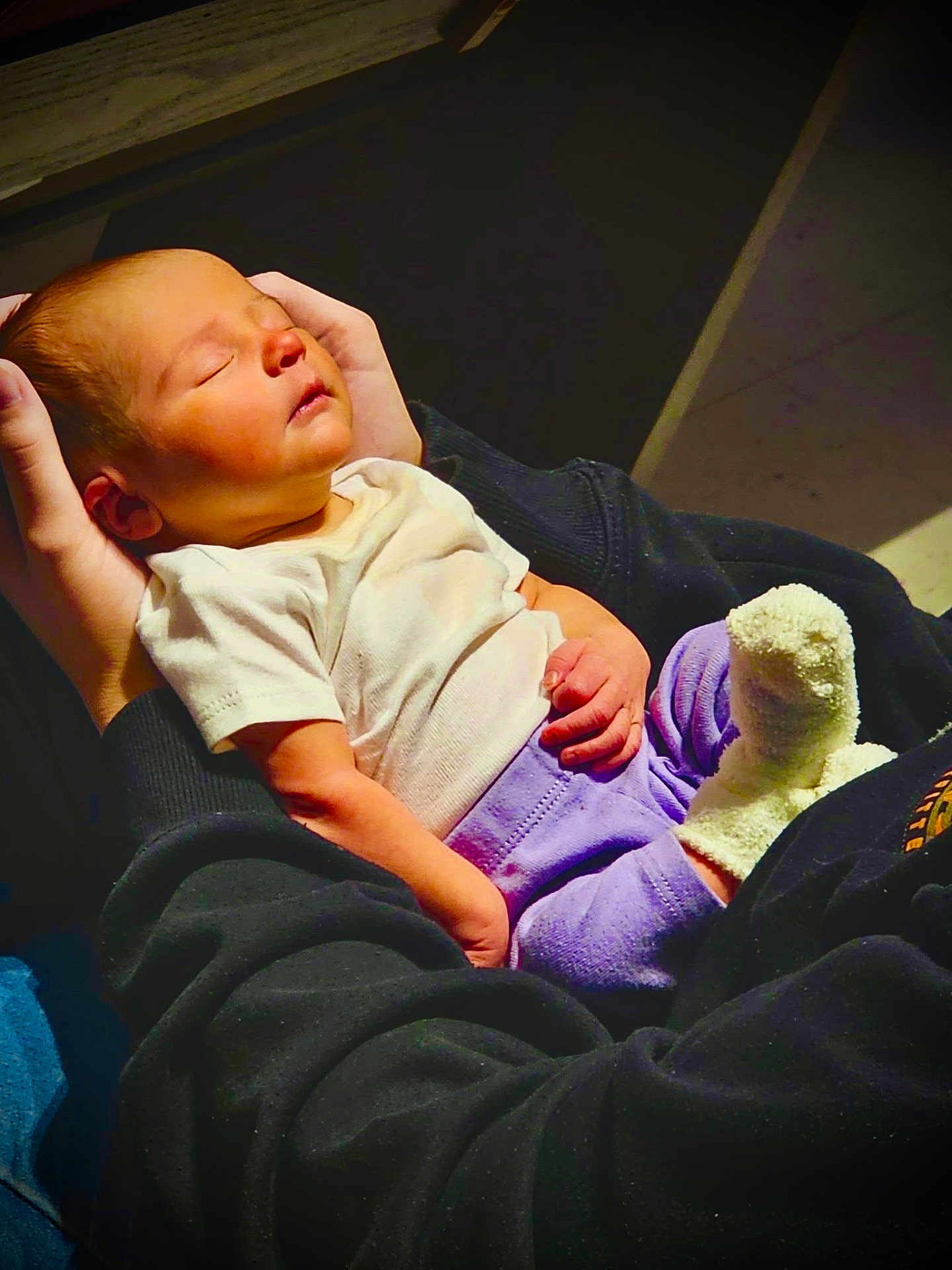 Mckenna joined the competition — help win amazing prizes! baby, infant, newborn, sleeping, cradled, adult_hands, onesie, white_shirt, purple_pants, sock, cozy, portrait, indoor, warm_light, lap, black_sweatshirt, peaceful, skin, floor_tiles, handheld