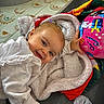 baby, blanket, child, clothing, colorful_ball, cozy, ear_piercing, eyes, face, floor_mat, hand, hardwood_floor, lying_down, play_mat, plush_blanket, portrait, smiling, toddler, toy, white_clothing