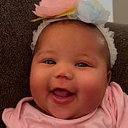 Trinity is registered to the contest to win money with this photo: baby, smiling, headband, flower, pink_clothing, couch, infant, happy, face, child, portrait, indoors, cute, closeup, cheerful, sitting, young, skin, person, toddler