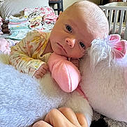 Harlow is registered to the contest to win money with this photo: baby, stuffed_animal, unicorn, toy, hand, bedroom, blanket, folded_clothes, nursery, person, infant, soft_toy, cute, child, indoor, sleepy, plush, furniture, pajamas, resting