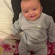 Denis is registered to the contest to win money with this photo: baby, smiling, infant, clothing, nike, gray_outfit, sitting, pillow, blanket, floral_pattern, indoor, cute, happy, child, portrait, apparel, young, person, comfort, cozy