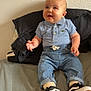 baby, child, polo_shirt, denim_pants, sitting, bed, shoes, black_shoes, white_shoes, curious, happy, indoor, casual_clothing, infant, cute, person, smiling, wall, textured_wall, comfortable