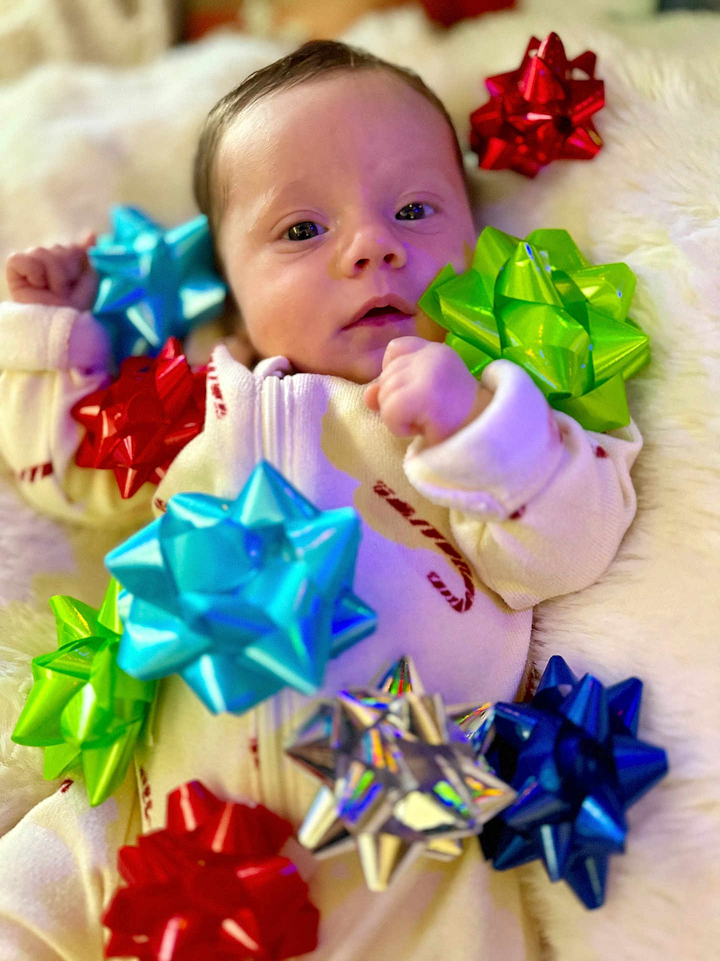 Kaia joined the competition — help win amazing prizes! baby, infant, face, person, gift_bows, colorful, decorations, holiday, cute, soft_texture, fluffy, white_background, clothing, lying_down, closeup, small_hands, expression, indoors, festive, cozy