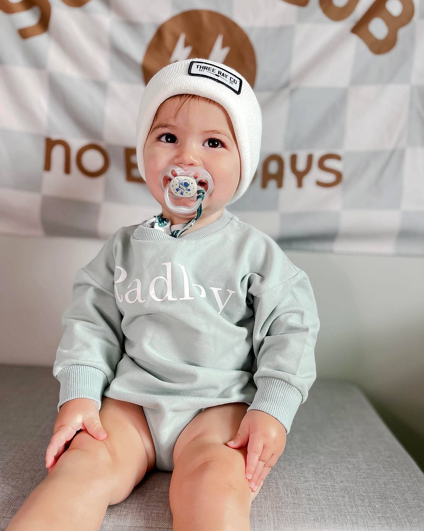 Radley joined the competition — help win amazing prizes! baby, baby_toddler_clothing, cap, child, collar, costume_hat, fashion_accessory, font, happy, headwear, human_leg, knee, logo, neck, person, portrait_photography, sitting, sleeve, smile, t_shirt