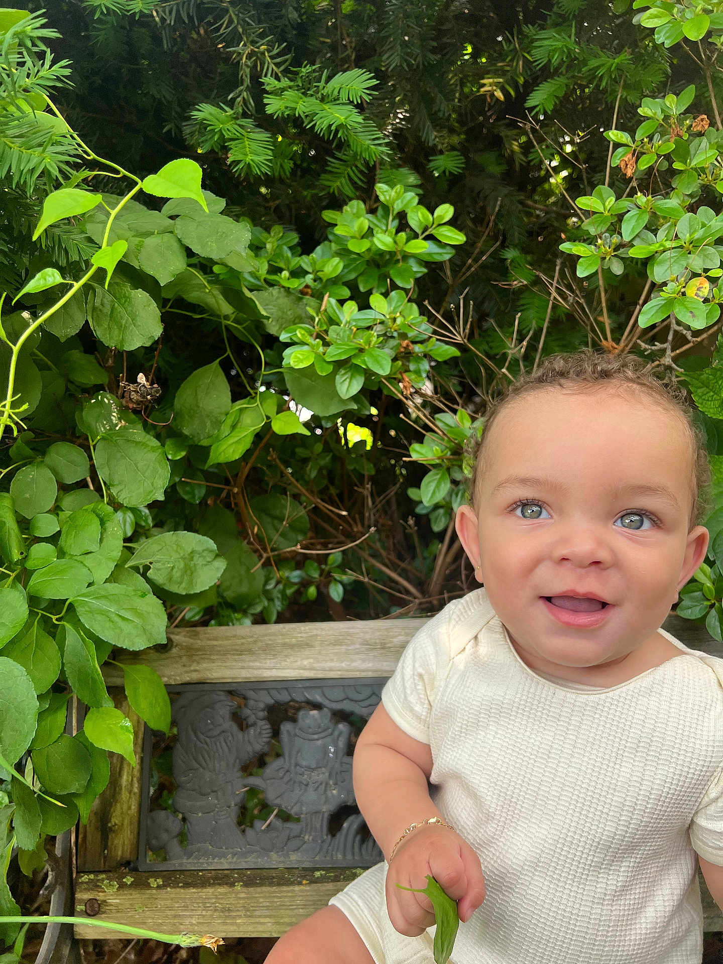 Eris G Hall joined the competition — help win amazing prizes! baby, child, smiling, outdoor, greenery, bench, leaf, curly_hair, cute, nature, plant, portrait, happy, toddler, skin, white_clothing, bracelet, sunlight, garden, face